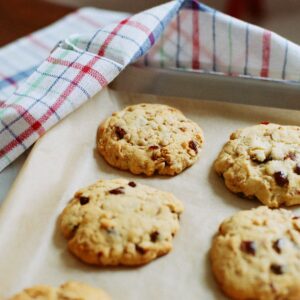 Close-up of freshly baked oatmeal raisin cookies cooling on a baking tray with a plaid towel.