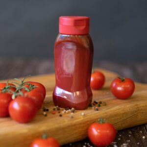Close-up of tomatoes and ketchup bottle on a wooden board with peppercorns.