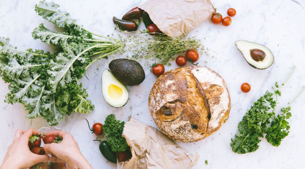 Fresh ingredients on a marble surface featuring bread, avocado, and vegetables for healthy eating.