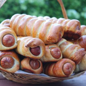 A close-up shot of freshly baked sausage rolls in a basket, outdoors.