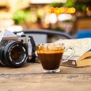 A warm espresso cup and vintage camera on a wooden table in an outdoor café setting.