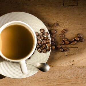 Top view of a cup of coffee on a wooden table with scattered beans.