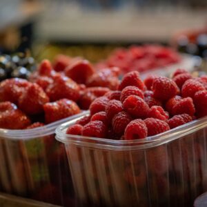 Close-up of fresh raspberries, strawberries, and cherries in plastic containers at a market.
