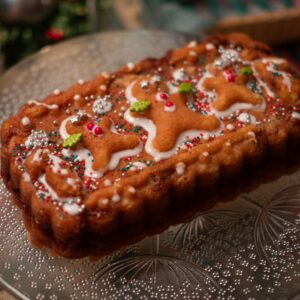 Delicious gingerbread cake topped with festive icing and sprinkles on a glass platter, perfect for holiday celebrations.