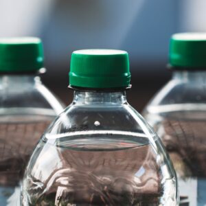 Focused view of three clear plastic bottles with green caps outdoors.
