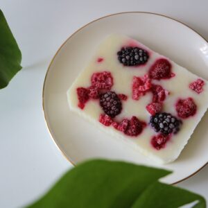 Frozen yogurt bar topped with raspberries and blackberries on a white plate, surrounded by leaves.