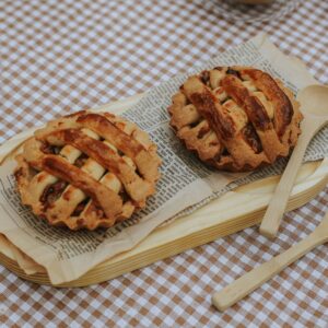 Rustic mini apple pies on a checkered tablecloth with wooden spoons and autumn leaves.
