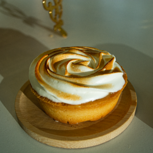 Golden brown lemon meringue tart with creamy topping on a wooden tray in natural light.