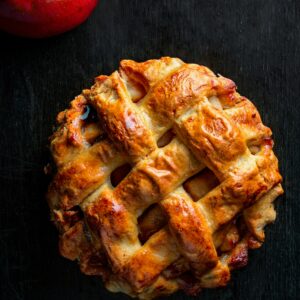Home Top view of a golden apple pie with a red apple on a dark background.