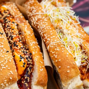 Two gourmet hot dogs with vibrant toppings and sesame seed buns.