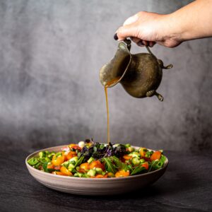 A vibrant salad being drizzled with dressing from a vintage jug, capturing healthy eating.