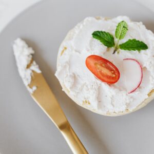 From above of delicious cottage cheese spread on bun decorated with vegetables and mint on round platter with golden knife placed on marble table