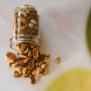 Assorted mixed nuts spill from a glass jar on a light surface, highlighting a variety of textures and colors.
