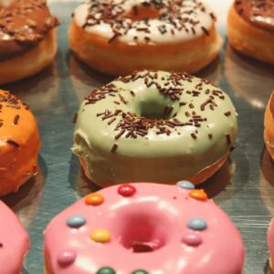 A close-up of various colorful iced donuts topped with chocolate sprinkles on a reflective surface.