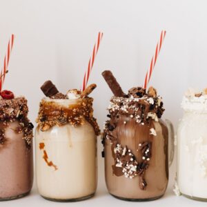 Close-up of four assorted milkshakes with various toppings in glass jars.