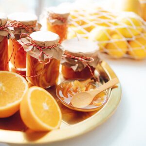 Homemade orange marmalade in jars beside sliced citrus fruits on a tray.