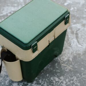 A green and beige cooler sits on a frozen ice surface, ideal for outdoor adventures.