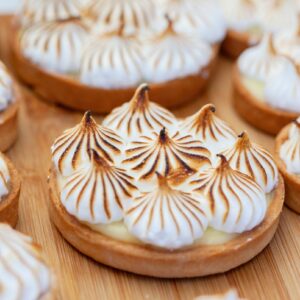 Close-up of freshly baked lemon meringue tartlets with golden peaks on a wooden surface.