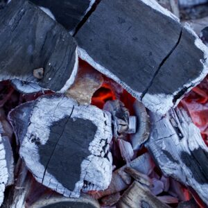 Detailed view of intense glowing charcoal embers with partially burned wood pieces.